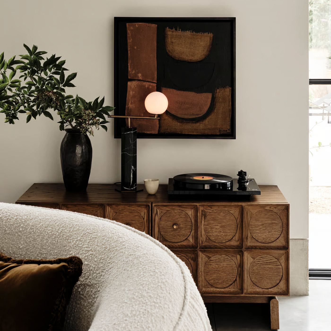 Mörkt träsideboard stylat med lampa, vas och tavla ovanför