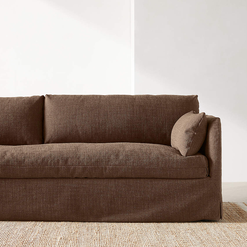 Brun soffa i mjuk textil mot ljus vägg och naturmatta